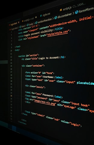 A close-up view of a computer screen displaying HTML and CSS code for a login form. The code includes elements like head, body, various input fields for username and password, and linked style sheets. The text is primarily in blue, white, orange, and green, set against a dark background.