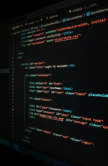 A close-up view of a computer screen displaying HTML and CSS code for a login form. The code includes elements like head, body, various input fields for username and password, and linked style sheets. The text is primarily in blue, white, orange, and green, set against a dark background.
