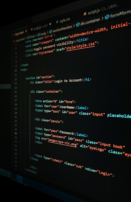 A close-up view of a computer screen displaying HTML and CSS code for a login form. The code includes elements like head, body, various input fields for username and password, and linked style sheets. The text is primarily in blue, white, orange, and green, set against a dark background.