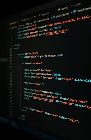 A close-up view of a computer screen displaying HTML and CSS code for a login form. The code includes elements like head, body, various input fields for username and password, and linked style sheets. The text is primarily in blue, white, orange, and green, set against a dark background.