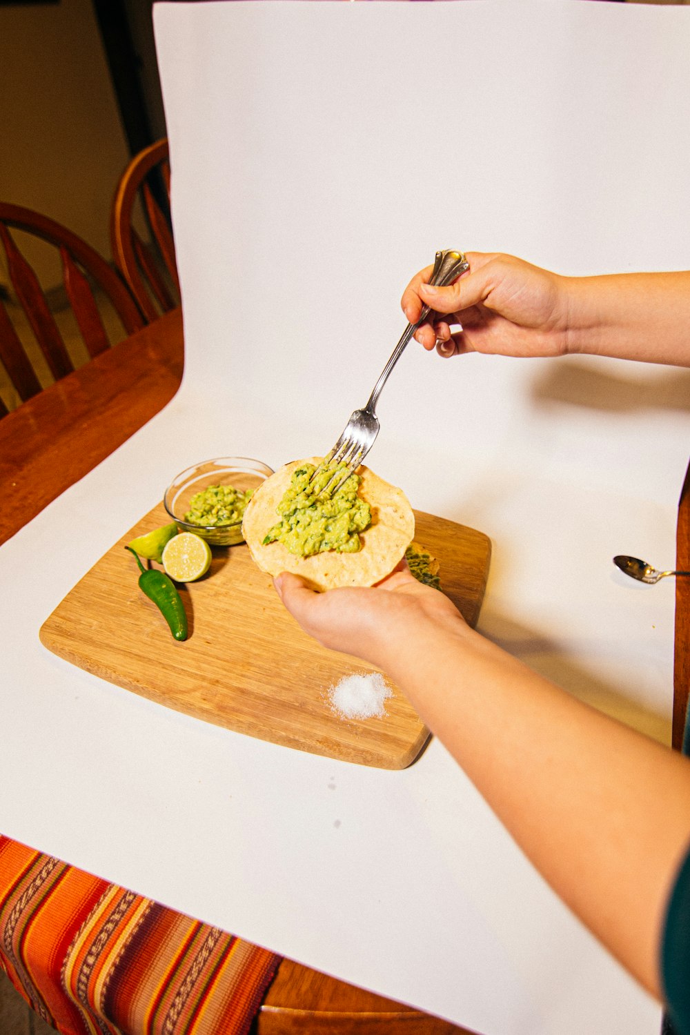 a person holding a fork over a tortilla on a cutting board