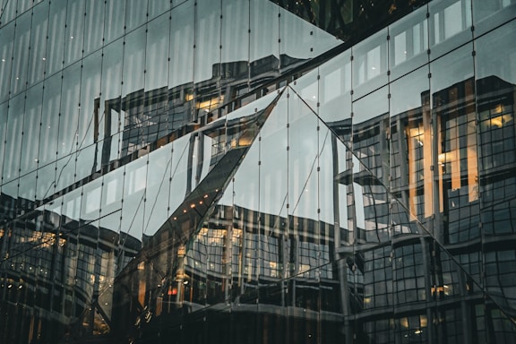 Reflections of a modern building on a glass facade, creating an abstract and geometric visual effect.