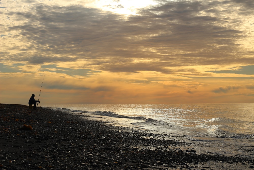 a man fishing on the beach at sunset