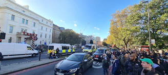 A journalist reporting live from a busy city street with police activity in the background.