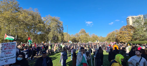 A vibrant rally with diverse supporters holding 'SA Victory Fund' signs under a sunny sky.