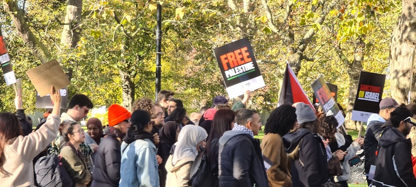 A diverse group of people gathered outdoors holding signs supporting justice for Palestine.