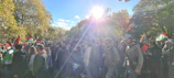 A lively crowd gathered around a speaker at an outdoor Flag and Torch Society event during golden hour.