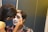A person is applying face paint on another person's face. The person receiving the makeup has a mostly white face with some black details being added. The scene appears to be in an indoor setting.
