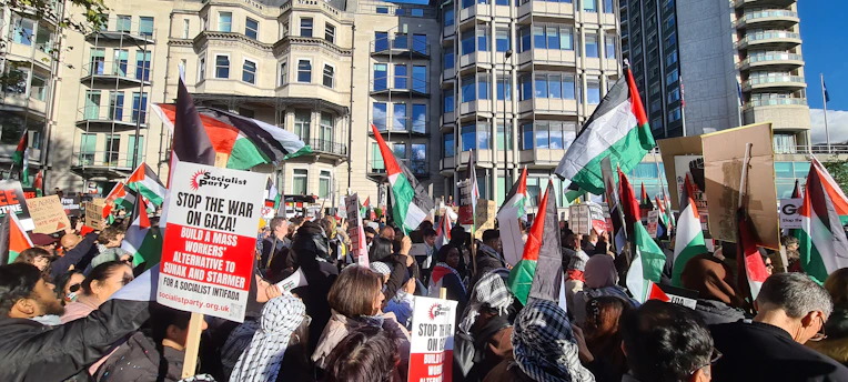 A determined crowd of South Sudanese people holding banners and flags, united in peaceful protest under a bright sky.