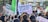 A crowded protest scene with many people holding up signs and banners. Prominent signs include phrases like 'Ceasefire Now!' and 'You Can't Hide, We Charge You With Genocide'. Flags and various protest placards are visible in the background.