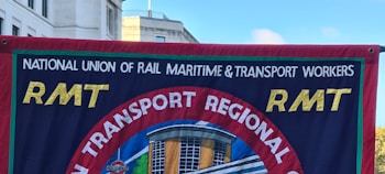 A banner displays the logo and name of the National Union of Rail, Maritime & Transport Workers, known as RMT. The banner's design includes bold yellow letters 'RMT' against a blue background with a central circular emblem showing a building and a blue-red contrast.