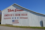 A white barn features bold red text that reads 'Bob Evans' and 'America’s Farm Fresh'. The barn is adorned with red and blue graphics including stars and a stylized American flag.