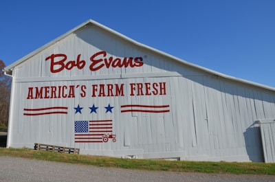 A white barn features bold red text that reads 'Bob Evans' and 'America’s Farm Fresh'. The barn is adorned with red and blue graphics including stars and a stylized American flag.