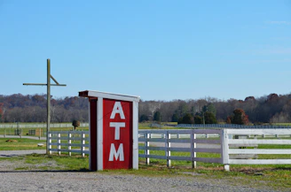 a red and white atm sign next to a white fence