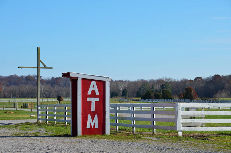 a red and white atm sign next to a white fence