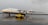 A large Antonov cargo aircraft is parked on a wet runway at an airport. It is white with blue and yellow accents and has four large jet engines. A yellow airport service vehicle is positioned in front of the plane.