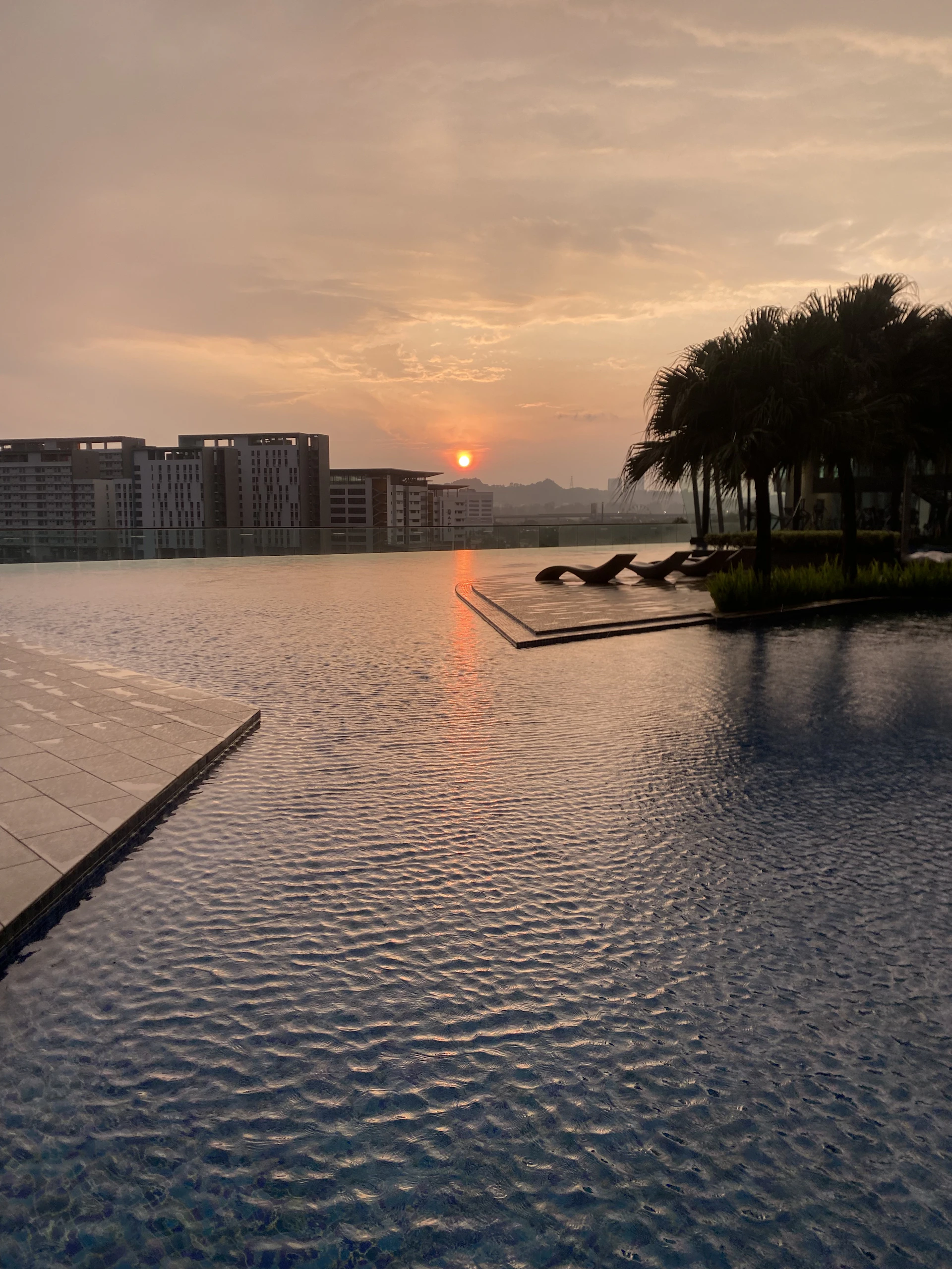 A serene sunset view over the Mihas Hotels and Resorts infinity pool, with warm burgundy and yellow hues reflecting on the water.