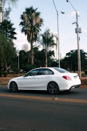 A sleek white sedan parked near a sunny Panjim street with palm trees.