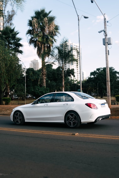 A sleek white sedan parked by a sunny beach road in Panjim with palm trees swaying in the background.