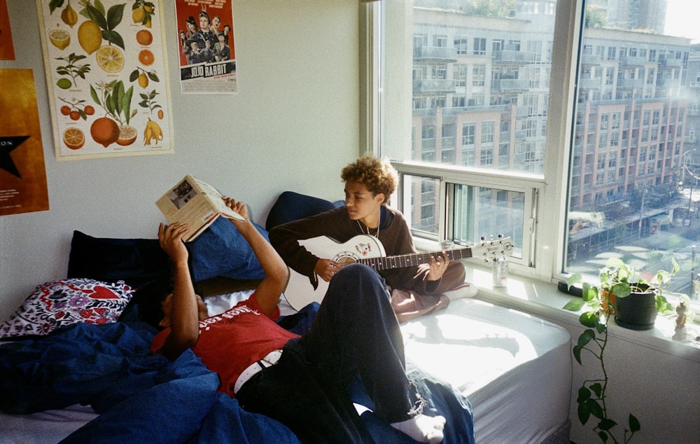 a young man sitting on a bed reading a book