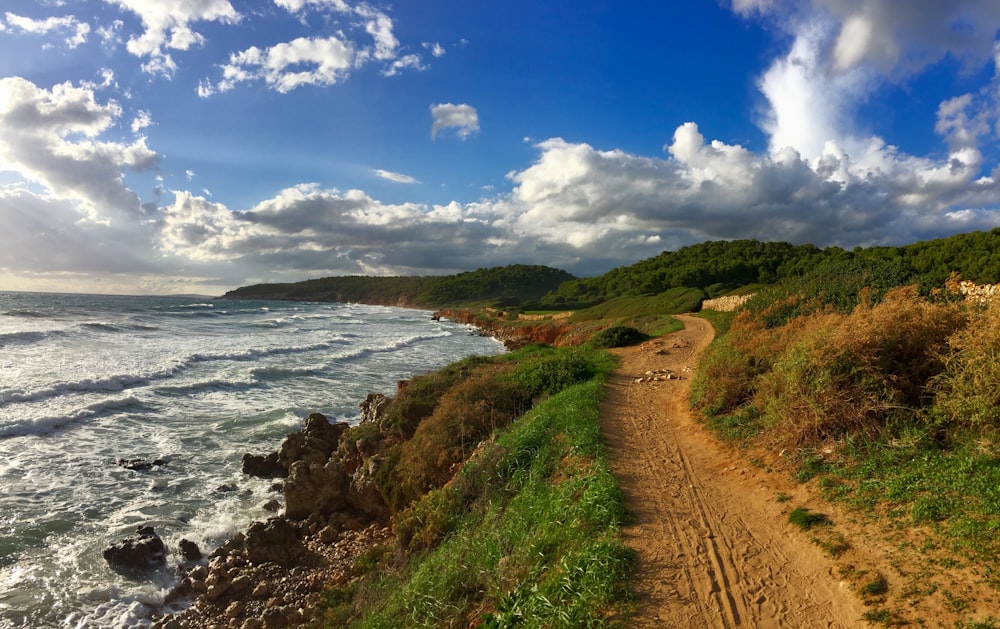 a dirt road next to the ocean under a cloudy sky