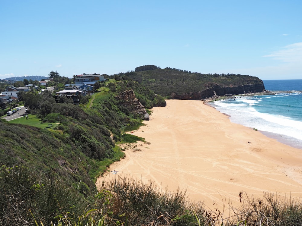 a sandy beach next to a lush green hillside