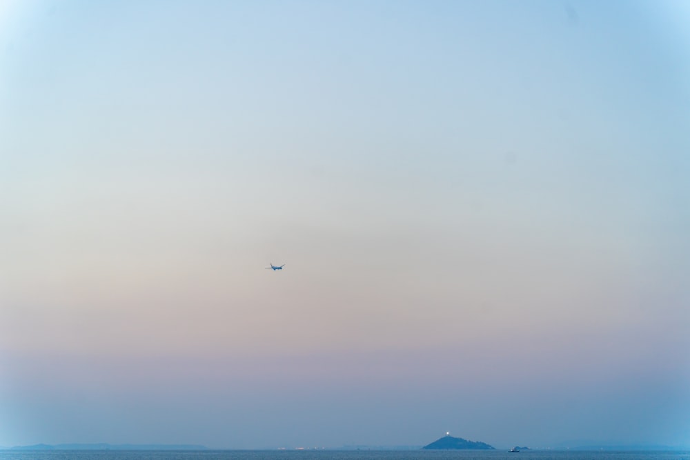 a plane flying over the ocean with a small island in the distance