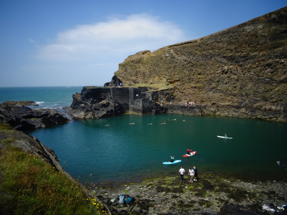 a group of people standing on top of a cliff next to a body of water