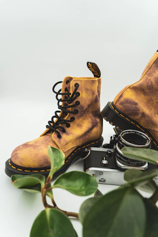 Pair of jungle shoes positioned on a wooden crate with military gear and an olive green helmet nearby.