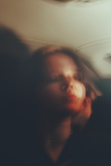 A blurry, artistic portrait of a person with soft, muted lighting. The image appears abstract with smooth blending of colors, giving it a dreamy and ethereal quality.