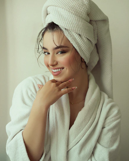 Portrait of a warm, smiling nail artist in a softly lit studio with beige and mocha tones.