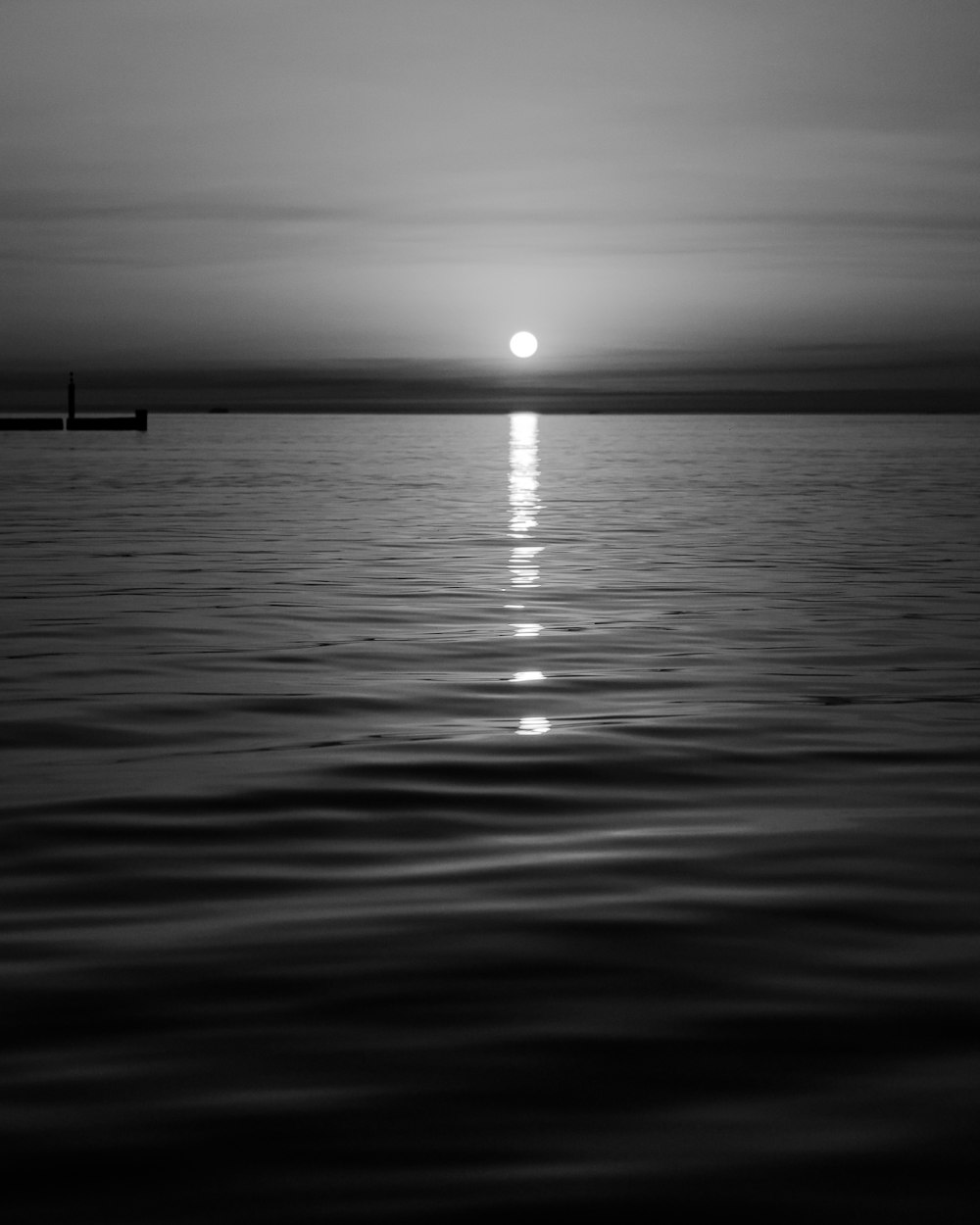 a black and white photo of the sun setting over the ocean