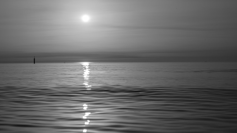 a black and white photo of the sun reflecting off the water