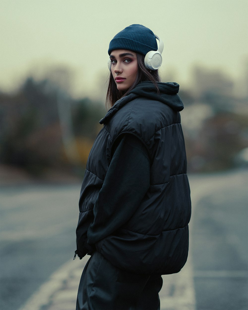 a woman standing on the side of a road wearing headphones
