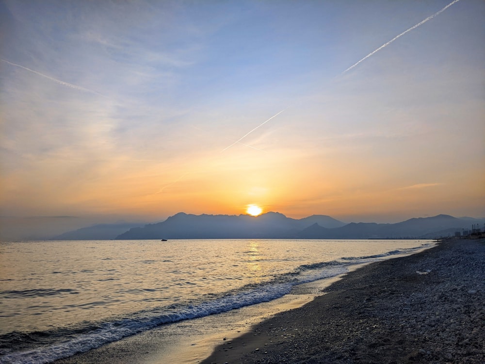 the sun is setting over the water at the beach