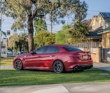 A gleaming red sedan parked in front of a cozy Buda neighborhood home on a sunny day.
