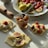 A marble countertop displays an artful arrangement of fresh figs, strawberries, and pastries with a small jar of fig preserves in the center. The pastries are topped with figs, strawberries, and cream, ready to be enjoyed. Light from perhaps a window casts soft shadows across the scene, highlighting the textures of the fruit and the dough.
