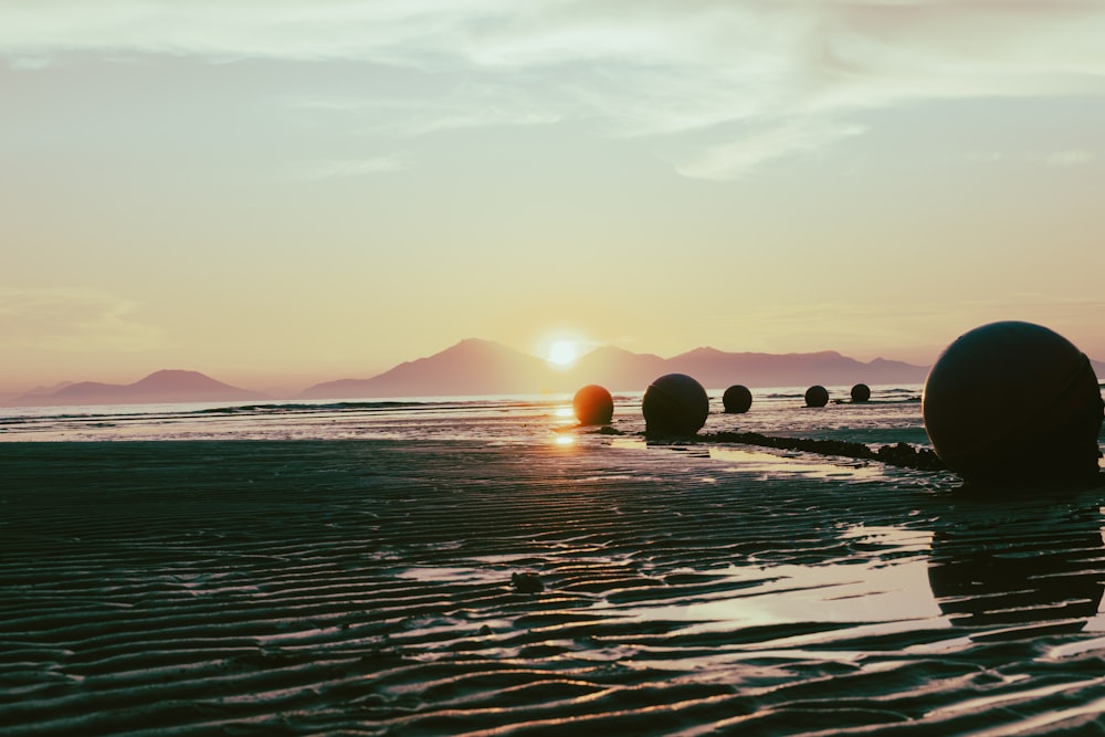 the sun is setting on the beach with balls in the water