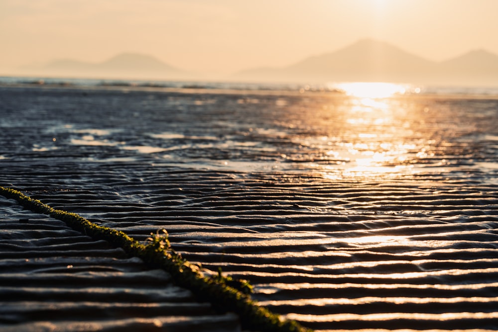 the sun is setting over the water and sand