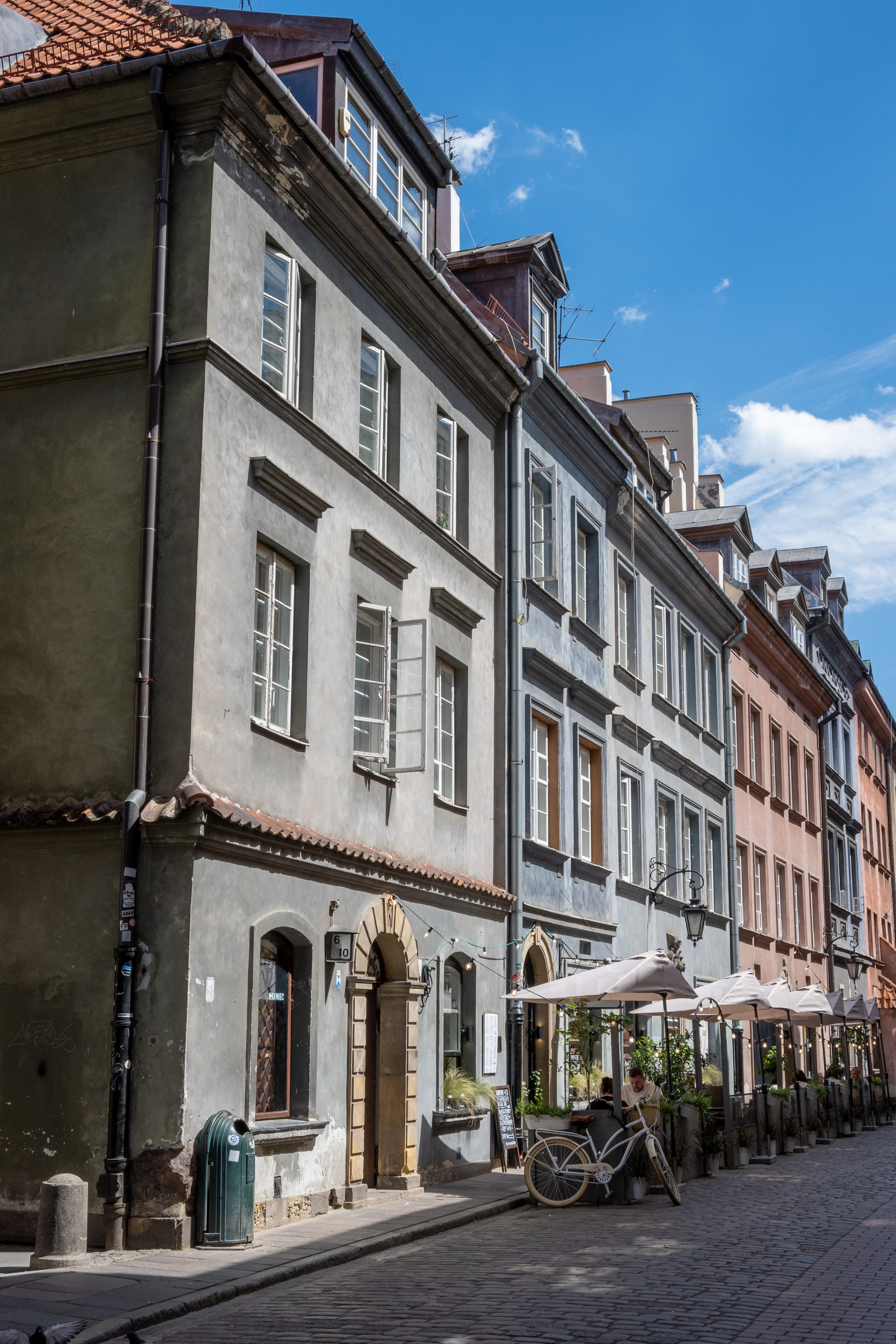 A narrow Old Town street lined with pastel townhouses, a cafe with umbrellas and a bicycle parked outside