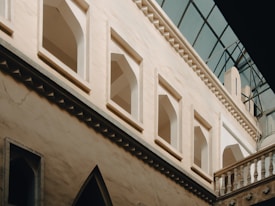 A view of an architectural structure with arched windows and a façade featuring intricate patterns. The walls are light-colored, and the roof is framed by a series of angular glass panes that allow natural light to illuminate the interior.