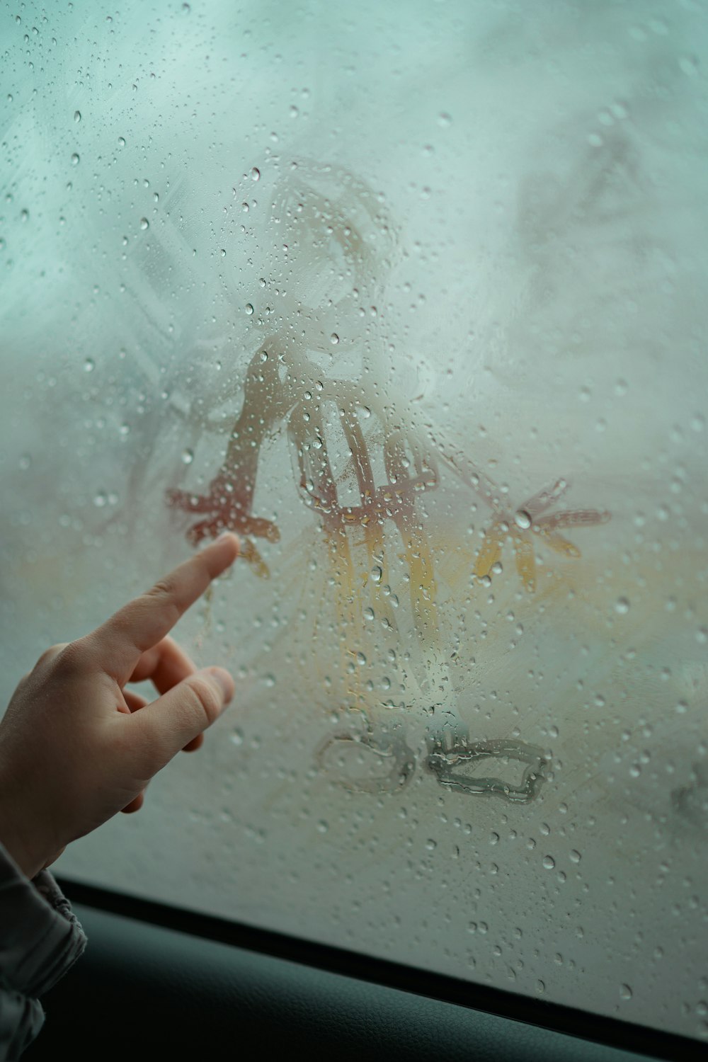 a person pointing at a window with rain drops on it