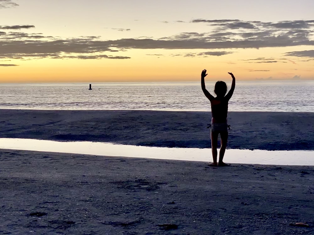 a person standing on a beach with their arms in the air