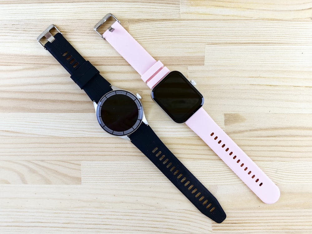 two smart watches sitting on top of a wooden table