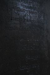 Dark, ancient script carved into a stone surface with low lighting casting shadows across the engraved characters.