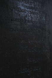 Dark, ancient script carved into a stone surface with low lighting casting shadows across the engraved characters.