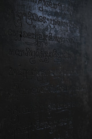 Dark, ancient script carved into a stone surface with low lighting casting shadows across the engraved characters.