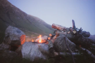 A cozy campfire surrounded by camping gear and a scenic backdrop of mountains.