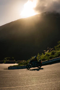 A motorcyclist riding through a winding mountain road in India during sunrise.