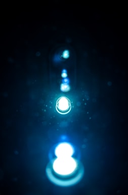 A series of glowing lights appear in a line, creating a sense of depth. The lights are surrounded by an ethereal glow with particles reflecting the light, set against a dark background.